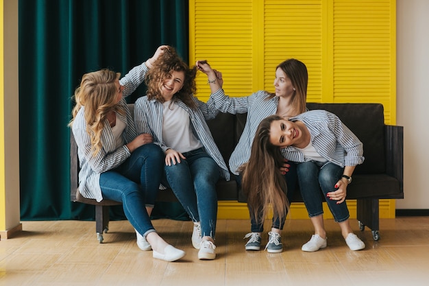 Quatro meninas em camisas listradas, jeans e tênis, posando no sofá. tiroteio em estúdio.