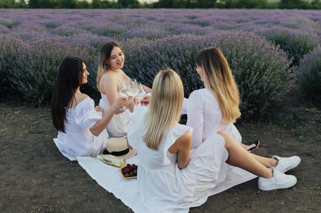 Quatro mulheres em vestidos brancos estão sentadas em um cobertor em um campo de lavanda.