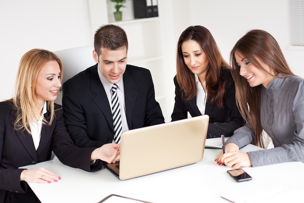 Quatro pessoas de negócios felizes olhando projeto no laptop no escritório.