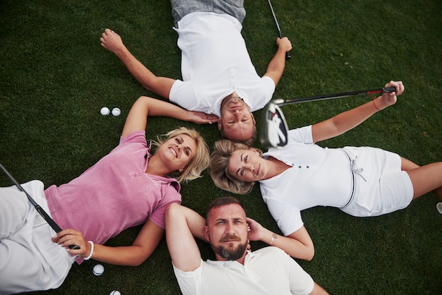 Quatro pessoas, dois homens e duas mulheres, deitam-se no campo de golfe e relaxam após o jogo