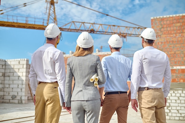 Quatro pessoas examinando com capacetes de segurança um novo objeto de construção