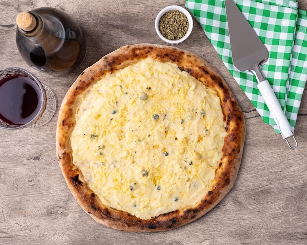 Foto quatro pizzas de queijo sobre mesa de madeira com vinho, orégano e espátula