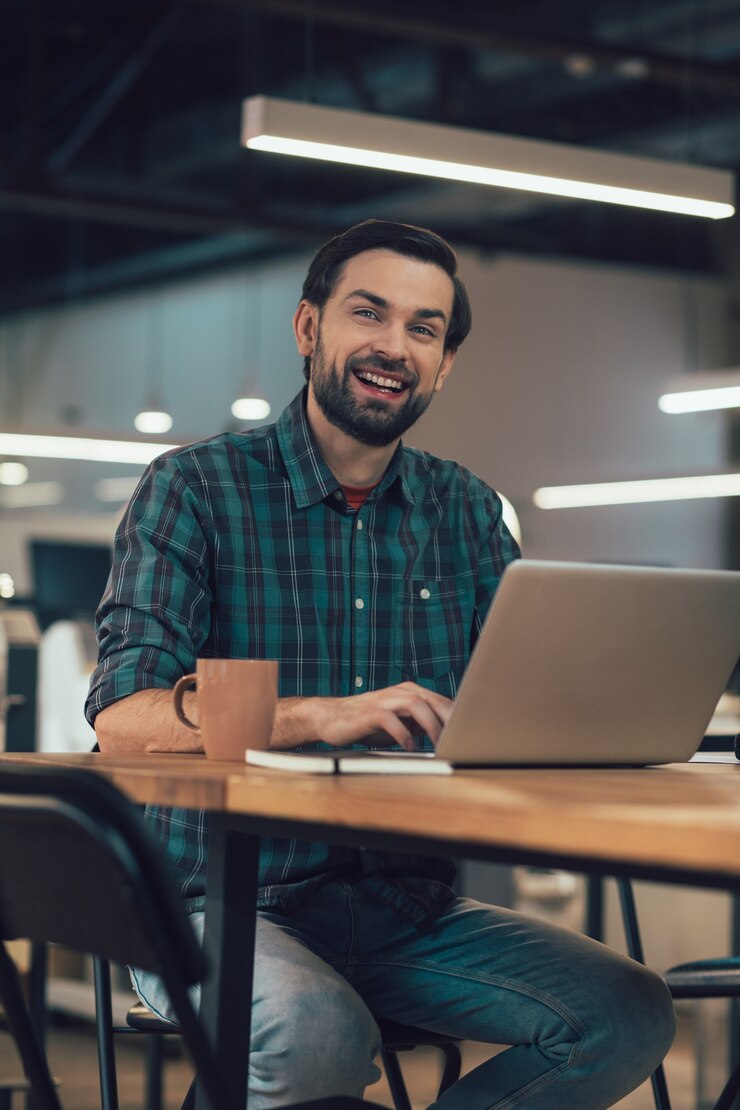 Que bom homem sentado à mesa com um laptop na frente dele