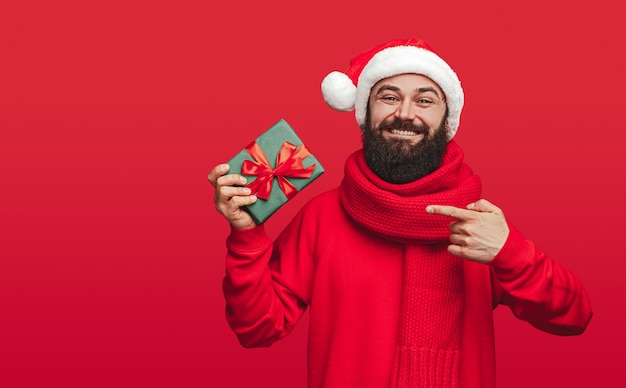 Que bom que homem barbudo com chapéu de Papai Noel sorrindo e apontando para o presente