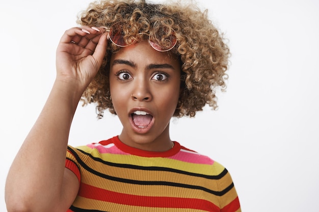 Que dices. Retrato de una mujer elegante y guapa sorprendida y sin palabras que hace estallar los ojos en la cámara por la mandíbula caída del asombro y la toma de gafas de sol de pie asombrado e impresionado