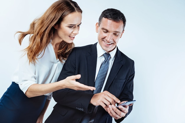 Qué es eso. Emprendedora sorprendida preguntando a su compañero de trabajo sobre algo mientras mira la pantalla de su teléfono inteligente durante su conversación.