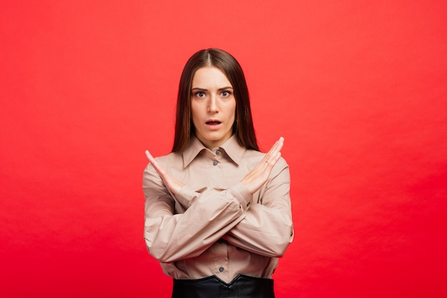 Qué es. El retrato femenino aislado en la pared roja. La joven mujer emocional enojada, asustada mirando a la cámara. Las emociones humanas, el concepto de expresión facial.