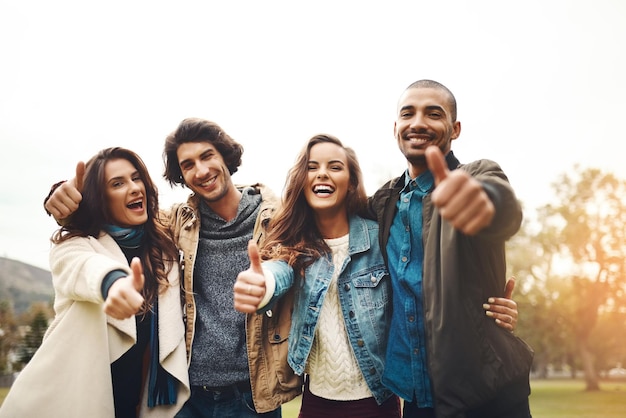 Qué gran día para pasar con amigos Retrato de un grupo de alegres jóvenes amigos acurrucados mientras muestran los pulgares hacia arriba afuera durante el día