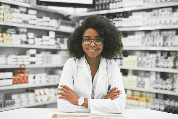 ¿Qué hay en el menú de hoy? Retrato de una joven y alegre farmacéutica parada con los brazos cruzados mientras mira la cámara en una farmacia.