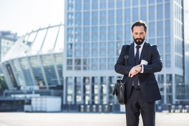 Qué hora es. Empresario de handsoem profesional yendo a trabajar mientras verifica el tiempo