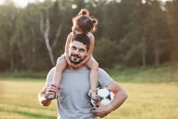 Que lindo tempo está hoje. Foto do pai com a filha em uma bela grama e bosque ao fundo.