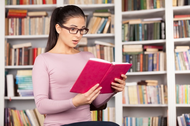 Que livro emocionante! Jovem surpreendida lendo um livro enquanto está sentada na biblioteca