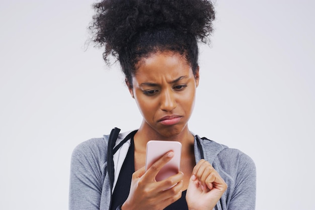 ¿Por qué no ha respondido todavía? Foto de estudio de una mujer joven que usa un teléfono móvil contra un fondo gris.