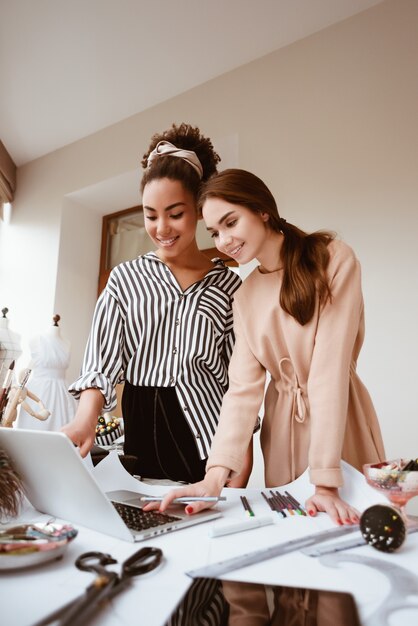 ¿Qué opinas de este vestido? Dos mujeres atractivas jóvenes que trabajan en un nuevo proyecto de diseño. Diseñador de mujer africana con morena joven mujer caucásica