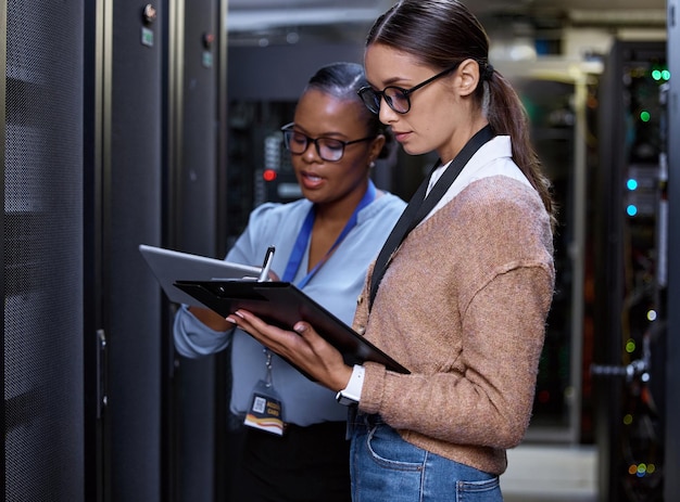 ¿Qué velocidades obtienes? Captura recortada de dos atractivas jóvenes programadoras de computadoras que trabajan juntas en una sala de servidores