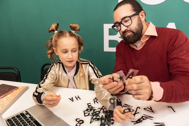 Foto quebra-cabeça de palavras. professor de cabelo escuro e barbudo usando óculos mostrando novas palavras para seu aluno