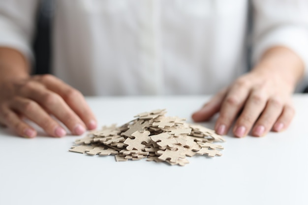 Quebra-cabeças espalhados na mesa e treinamento de negócios de mãos femininas e conceito de quebra-cabeça