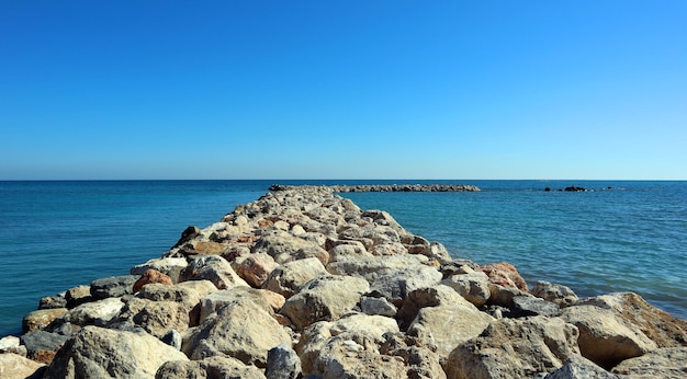Quebra-mar de grandes pedras no mar azul ao horizonte, estrada ao mar, bela paisagem marítima, Mediterrâneo
