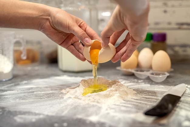 Quebrando ovos com as mãos das mulheres em farinha para fazer massa para bolos