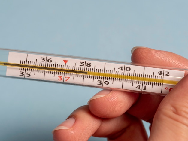 Quecksilberthermometer in der Hand einer Frau lokalisiert auf einem blauen Hintergrund.