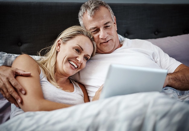 Quedarse en casa y relajarse Toma de una pareja madura usando una tableta digital mientras está acostado en la cama