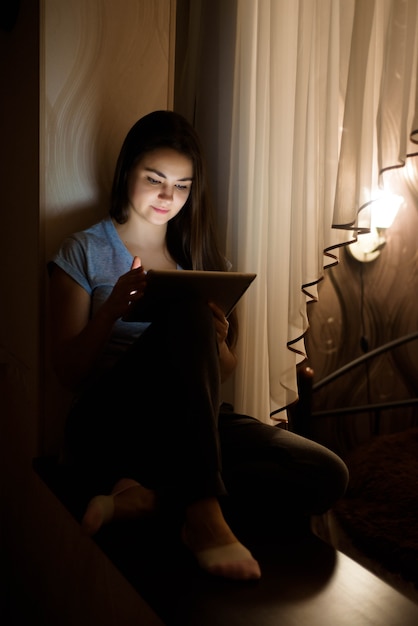 Quedarse en casa. Trabajar en casa. Mujer joven sentada junto a la ventana y usando tableta digital en casa.
