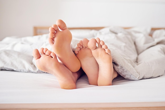 Quedémonos en la cama hoy Foto de los pies de una pareja asomando por debajo de un edredón