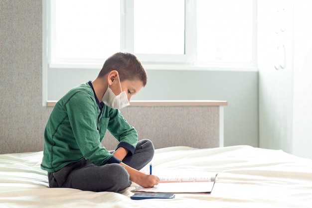 Quédese en casa para prevenir la pandemia de coronavirus de cuarentena. Un niño enmascarado aprende lecciones durante el período de cuarentena. Prevención de epidemias. COVID-19.