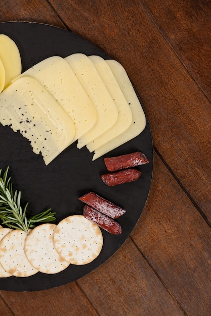 Foto queijo, alecrim, linguiça e biscoito na placa de ardósia