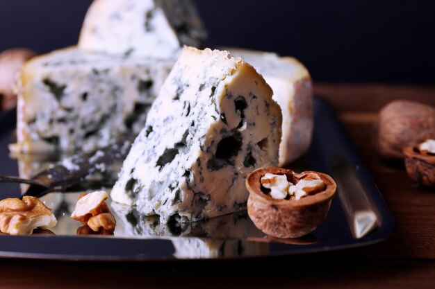 Queijo azul com nozes e lâmina na bandeja de metal e mesa de madeira e fundo escuro