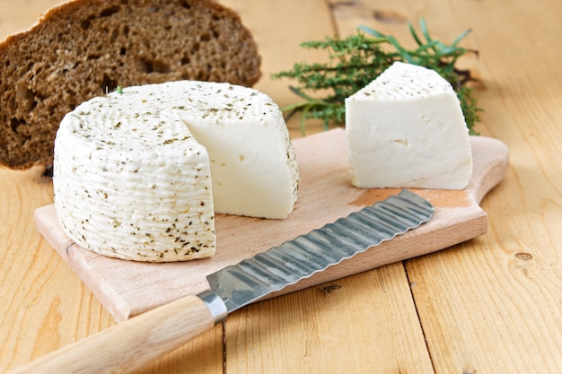 Queijo branco e pão em um fundo de madeira e verdes