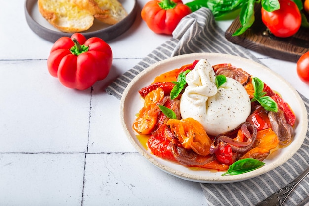 Queijo burrata com tomate assado pimenta cebola vermelha e manjericão fresco sobre fundo de azulejo branco