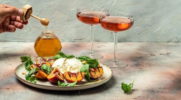 Queijo burrata e pêssegos grelhados com manjericão e pinhões Dois copos de vinho rosé sobre um fundo claro Delicioso antepasto para a vista superior do texto