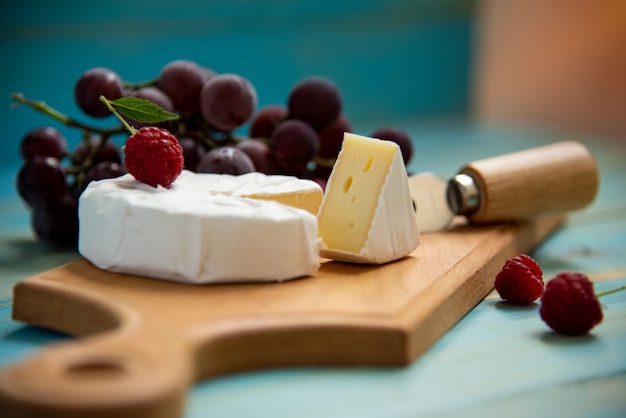 Queijo camembert com framboesas e uvas em um fundo azul