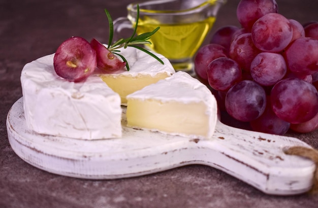 Queijo camembert e uvas em uma placa de madeira branca.