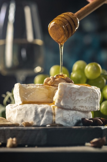 Queijo camembert ou brie caseiro orgânico em uma placa de madeira com uvas, nozes e mel. Estilo rústico.