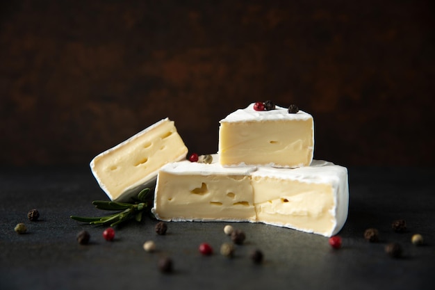 Foto queijo camembert ou brie com alecrim e pimenta no fundo escuro de pedra. copie o espaço. foto de estúdio.