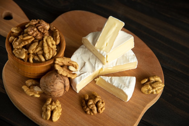 Foto queijo camembert ou brie com miolo de noz na tábua em fundo escuro de madeira.