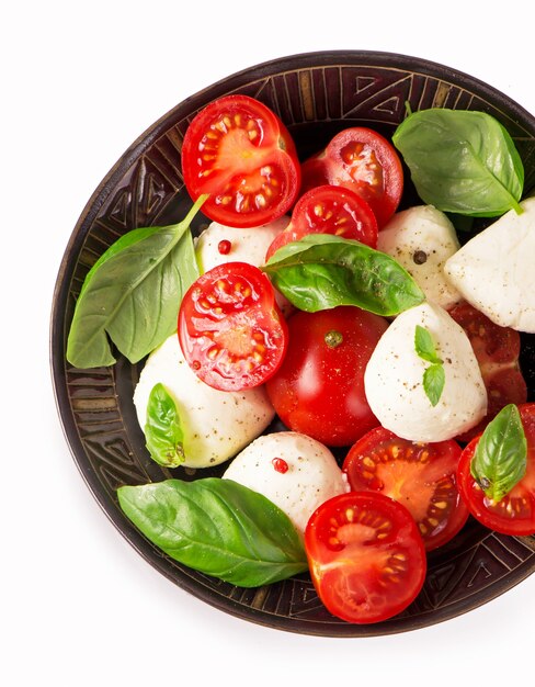 Queijo camembert redondo com tomate cereja e manjericão em um prato escuro