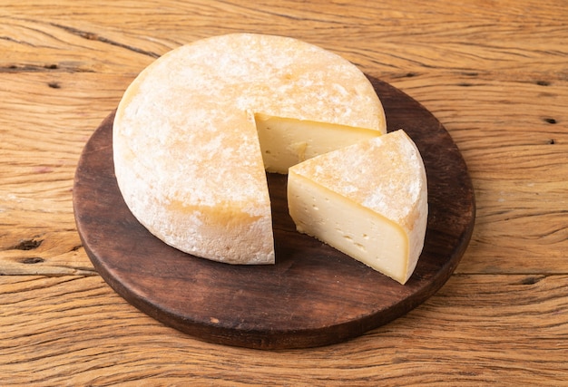 Foto queijo canastra artesanal de minas gerais, brasil, sobre tábua de madeira com pedaço cortado.