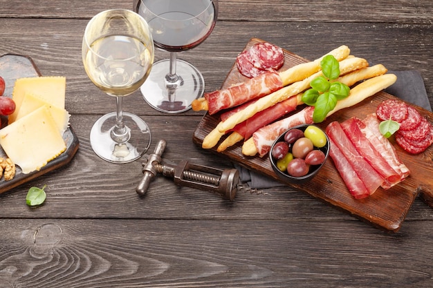 Queijo carne Uvas e azeitonas antepasto Tabuleiro de seleção de aperitivos e copos com vinho tinto e branco