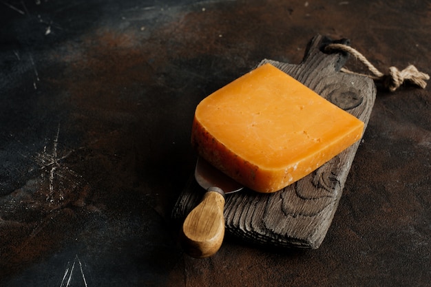 Queijo cheddar em uma placa de madeira sobre um fundo escuro.