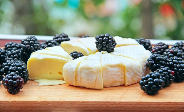 Queijo com mirtilos em uma tábua de madeira Queijo em fatias com bagas