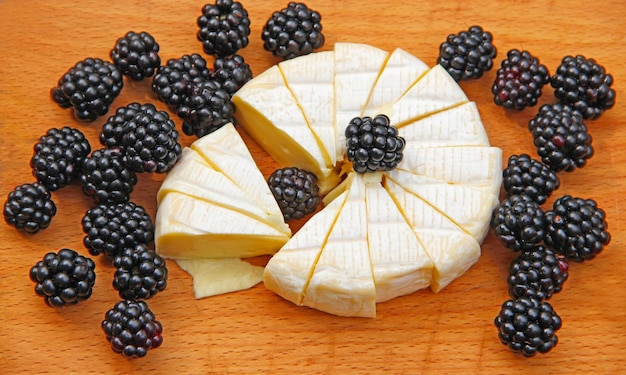 Queijo com mirtilos em uma tábua de madeira Queijo em fatias com bagas