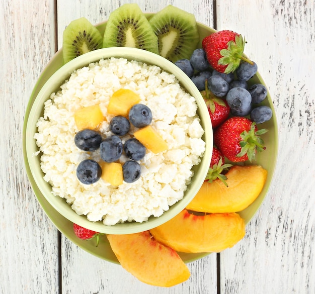 Queijo cottage com frutas e bagas em tigela na mesa de madeira