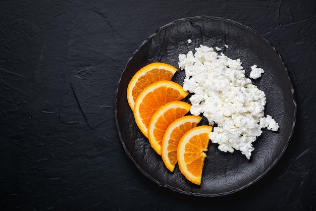 Queijo cottage com laranja em um prato sobre uma mesa preta