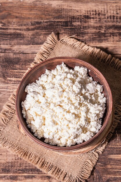 Queijo cottage em uma tigela de cerâmica. Produto lácteo caseiro em um prato fundo. Mesa de madeira velha, vista de cima