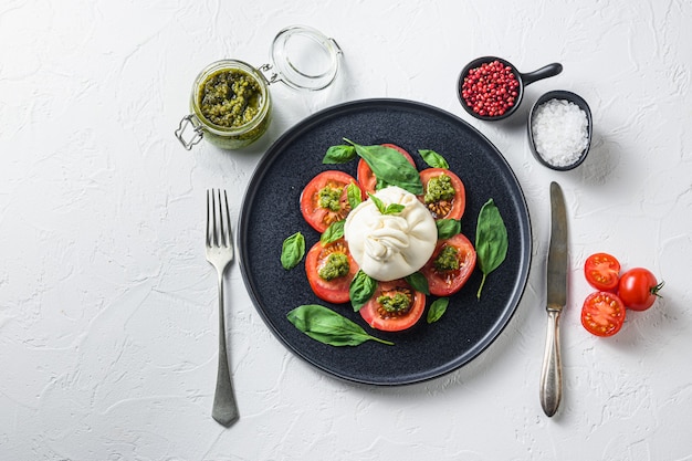 Queijo de burrata de búfala servido com tomates frescos e folhas de manjericão com molho pesto em prato preto