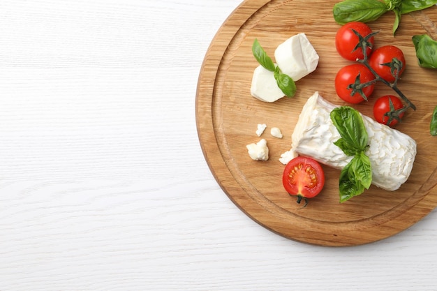 Queijo de cabra delicioso com manjericão e tomate na vista superior da mesa de madeira branca Espaço para texto