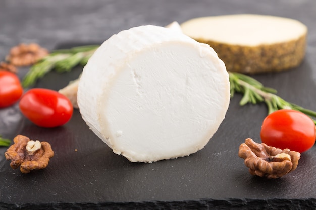 Queijo de cabra e vários tipos de queijo com tomate na placa de ardósia preta sobre fundo preto de concreto